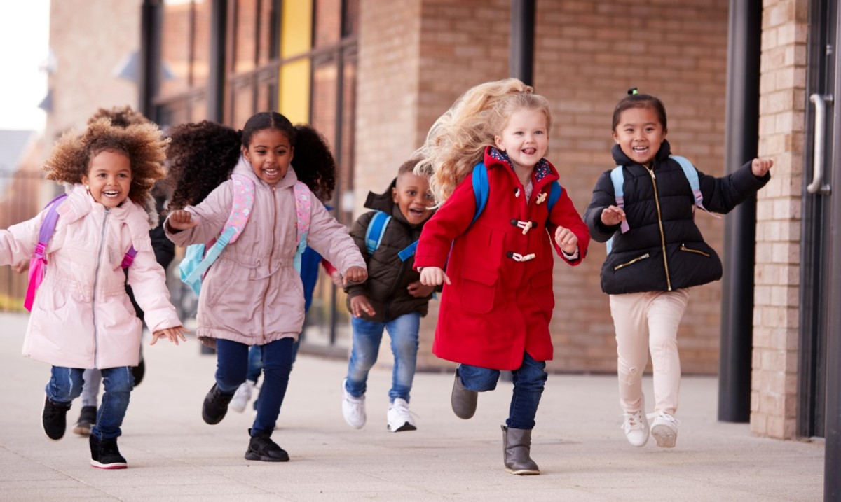 Group of happy children aged 5 to 9 running with school bags on their backs